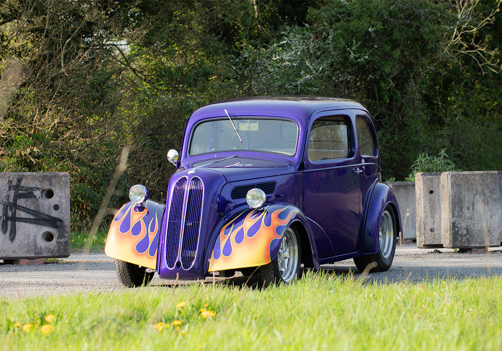 purple ford pop hotrod on a grassy industrial road 